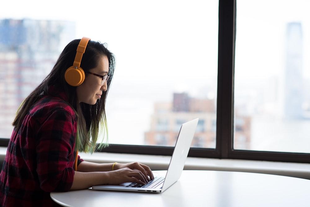 A person wearing headphones working at a laptop by a window