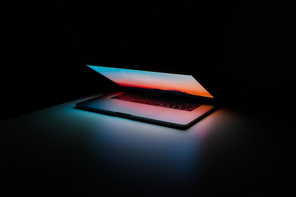 A glowing laptop open in a darkened room