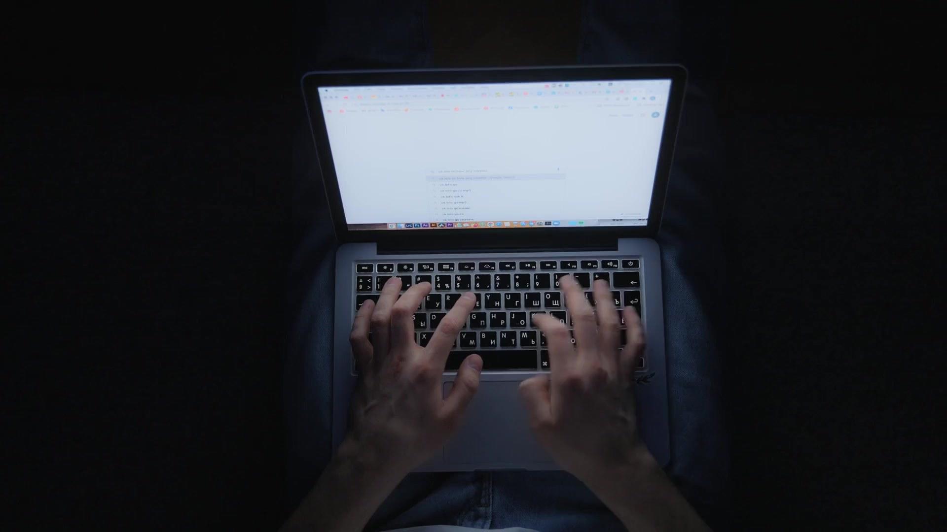 Hands typing on a laptop late at night, lit only by the screen