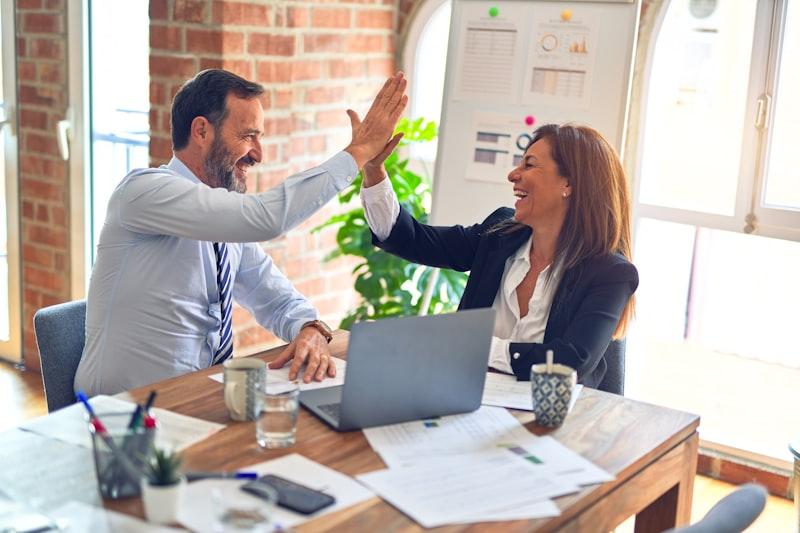 Two colleagues high-fiving across a desk after reaching a decision